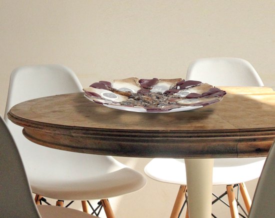 Decoratieve fused glas schaal met bruine en crèmekleurige segmenten op een ronde houten tafel met witte stoelen.