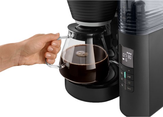 Een hand pakt een glazen koffiekan met vers gezette koffie uit een zwarte koffiezetapparaat.