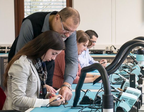 Docent helpt leerlingen met een soldeerproject in een klaslokaal.
