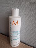 Witte Moroccanoil Hydrating Conditioner fles met oranje M-logo op een houten ondergrond.