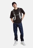 Man met donkerblauwe G-Star Mosa Straight jeans, zwart T-shirt met print, zwarte muts en witte laarzen.