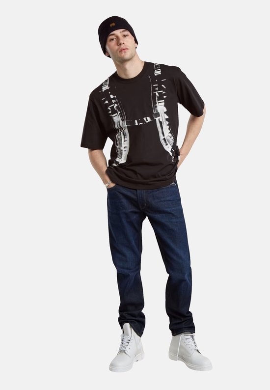 Man met donkerblauwe G-Star Mosa Straight jeans, zwart T-shirt met print, zwarte muts en witte laarzen.