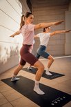 Twee vrouwen doen yoga in een blauwe en bordeauxrode nauwsluitende sportlegging.
