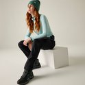 Zittende vrouw met rode haren, draagt een lichtblauwe gestreepte longsleeve, zwarte hikingbroek en groene muts.