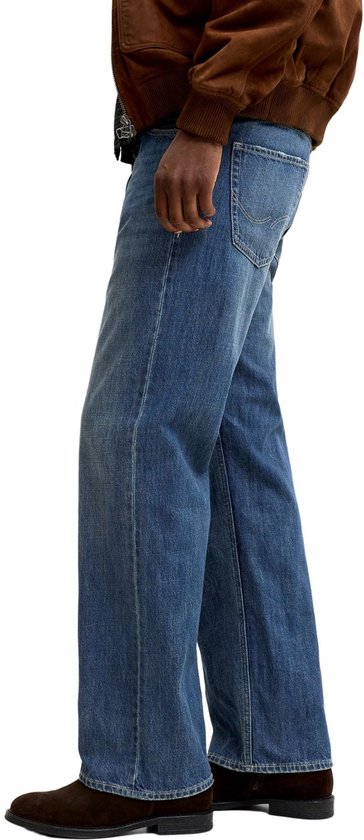 Man met de hand in de zak van een wijde blauwe jeans, zijkant gezien.