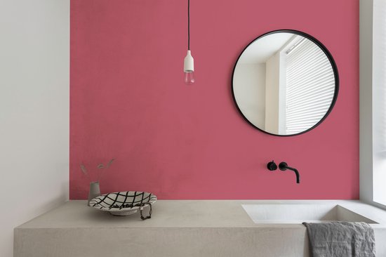 Een badkamer met een roze muur, een betonnen wastafel met zwarte kraan en een ronde spiegel met zwart frame.