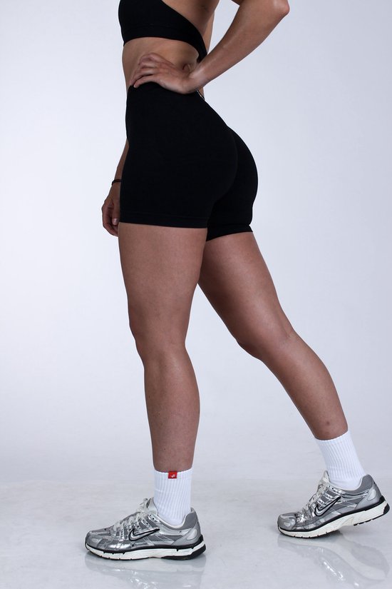 Vrouw in zwart sportbroekje en zilveren sneakers met witte sokken. Ze staat met haar hand op haar heup.