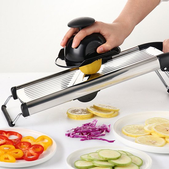 Mandoline snijdt citroen in dunne plakjes, met gesneden paprika, rode kool en courgette op schotels.