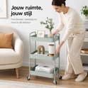 Chariot de cuisine vert menthe dans un salon avec des objets décoratifs et des livres, utilisé par une femme.