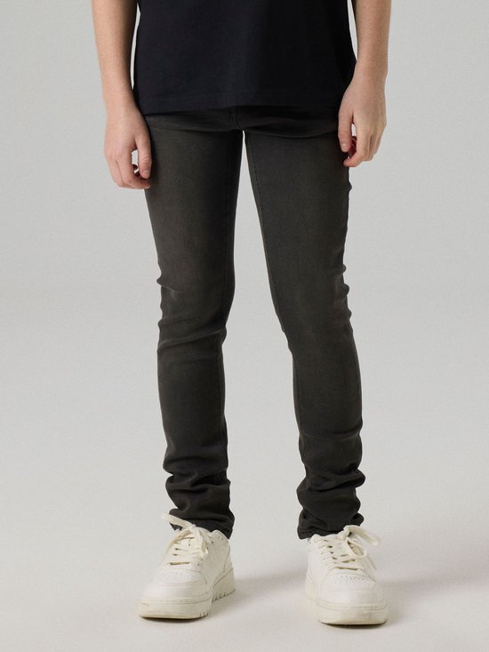 Jongen in een grijze slim fit spijkerbroek, met witte sneakers.