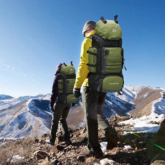 Twee wandelaars met grote groene en zwarte trekking rugzakken in een besneeuwd berglandschap. Rugzakken met volume 90L en XL.