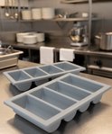 Twee grijze bestekbakken met vier vakken op een roestvrijstalen tafel in een keuken.