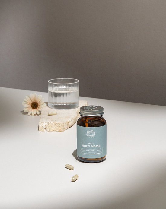 Bruine pot met mintgroen label "Mattisson HEALTHSTYLE VEGAN MULTI MAMA" naast een glas water en twee capsules.