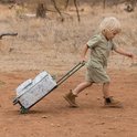Jongetje met blonde haren in safari-kleding trekt een koffer met safari print door droog gras.