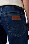 Donkerblauwe Wrangler jeans met bruin lederen logo op de achterzak en kenmerkend stiksel. Gecropte foto van de achterkant.