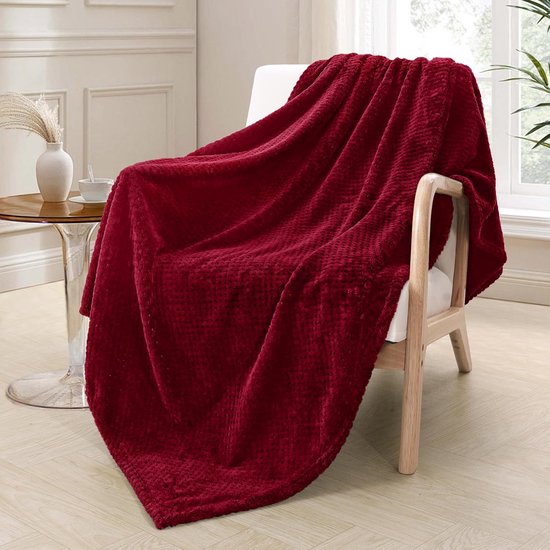 Bordeauxrode fleece deken gedrapeerd over een witte stoel bij een raam.
