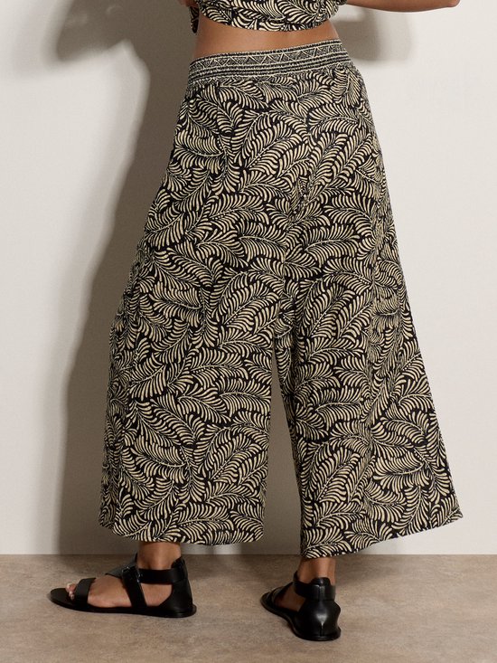 Detail van de culotte met wijde pijpen, zwarte en beige bladprint en zwarte sandalen.