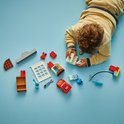 LEGO Duplo onderdelen: rode Lightning McQueen auto, garage, doktersspullen en gereedschap, uitgestald op blauwe ondergrond.