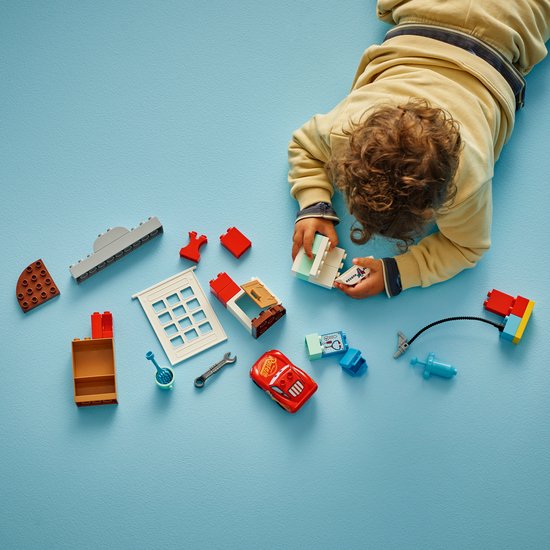 LEGO Duplo onderdelen: rode Lightning McQueen auto, garage, doktersspullen en gereedschap, uitgestald op blauwe ondergrond.