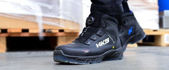 Man met zwarte veiligheidsschoenen met HKS logo, staand op een pallet.