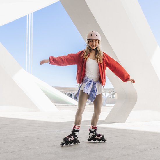 Meisje in rood jack, roze helm en zwart-roze skeelers met witte streepjes sokken.