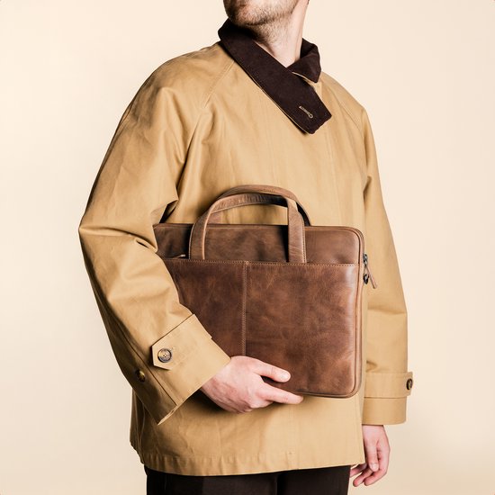 Man in een trenchcoat met een bruine leren laptoptas aan zijn zijde.