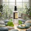Fles COSRX Advanced Snail 96 Mucin Power Essence te midden van natte stenen en planten.