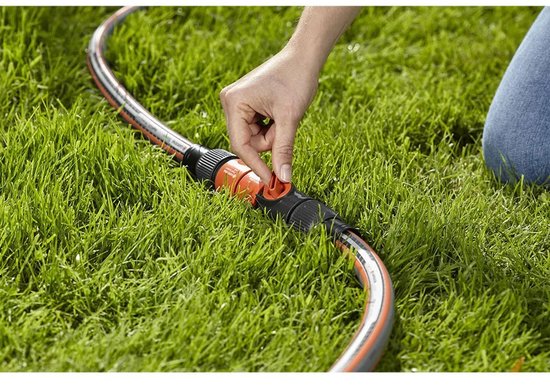 Een hand met oranje en zwarte tuinslangkoppeling met hendel, in groen gras.