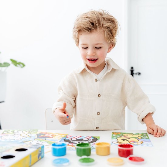 Jongetje met blonde krullen, met blauwe verf op duim. Potjes met rode, gele, groene en blauwe verf.