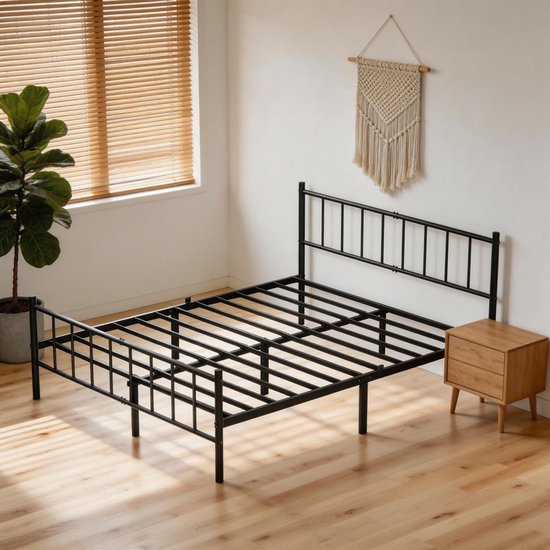 Leeg zwart metalen bedframe met lattenbodem in een minimalistisch interieur met een houten nachtkastje en een plant.