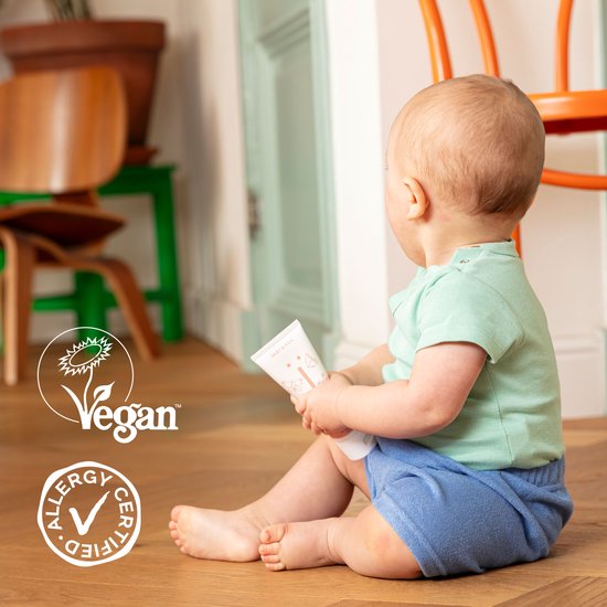Baby zittend op de grond met een Naïf tube, Vegan en Allergy Certified keurmerken.