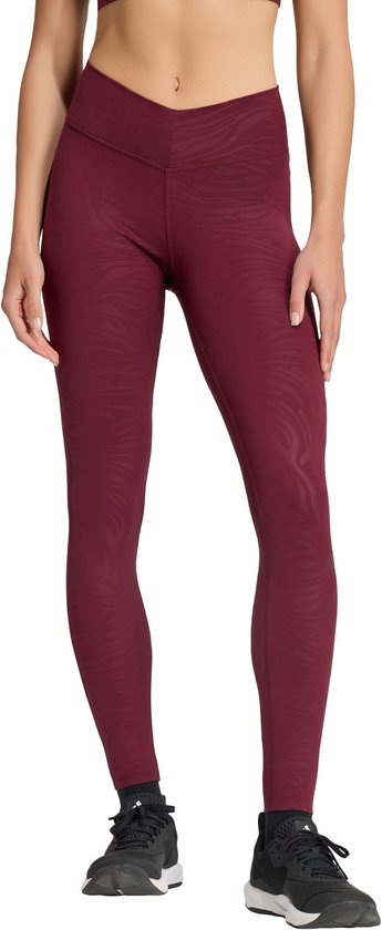 Vrouw in een bordeauxrode legging met tijgerprint en zwarte sportschoenen.