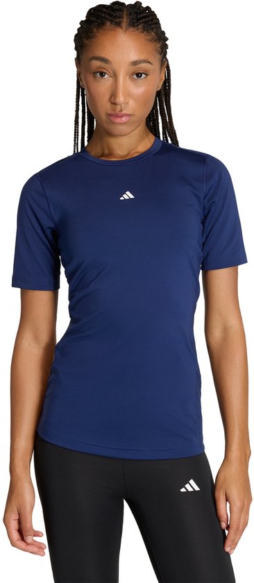 Vrouw met donkerblauwe Adidas Techfit trainingstop met korte mouwen en wit logo, met zwarte legging.