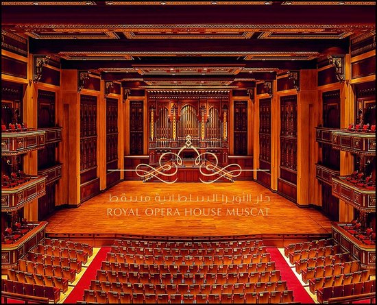 Luxe interieur van het Royal Opera House Muscat met houten panelen, een pijporgel en rode stoelen in een theateropstelling.