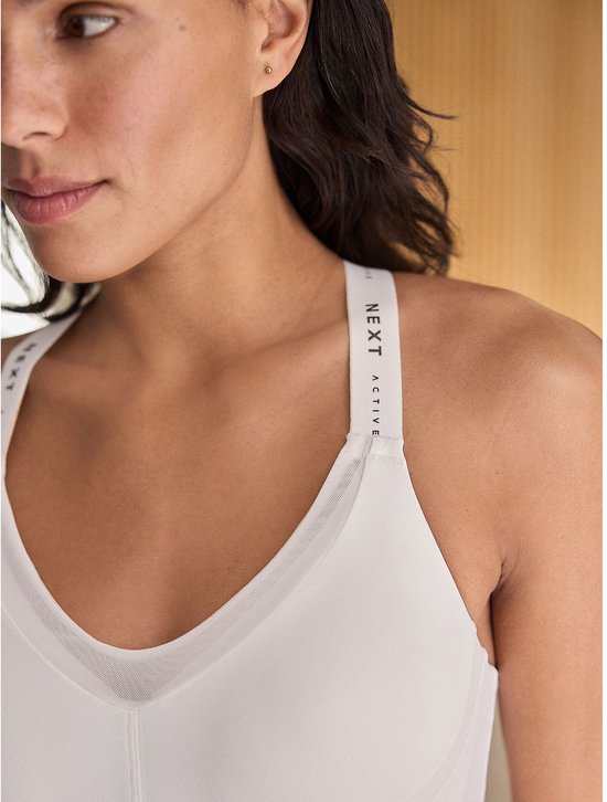 Detail van de zijkant van een witte sportbeha met mesh-inzetstukken en een logo.