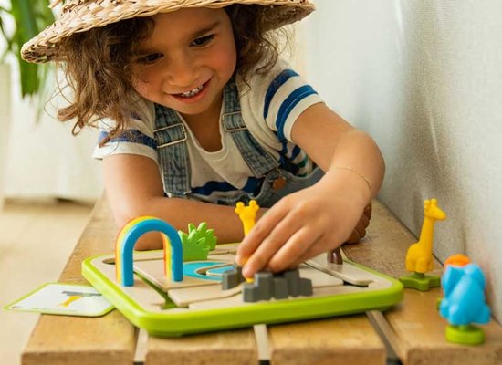 Meisje met strooien hoed speelt safarispel met miniatuur dieren en een regenboogbrug.