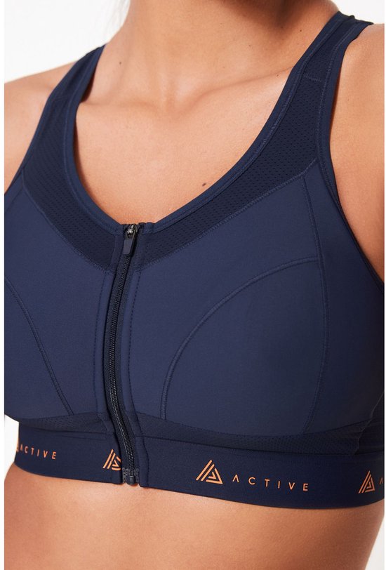 Close-up van marineblauwe sportbeha met rits vooraan, mesh inzetstukken en oranje 'ACTIVE' band.