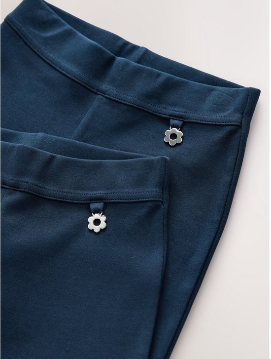 Twee donkerblauwe broeken in close-up, met een bloemvormig knoopdetail op de tailleband.
