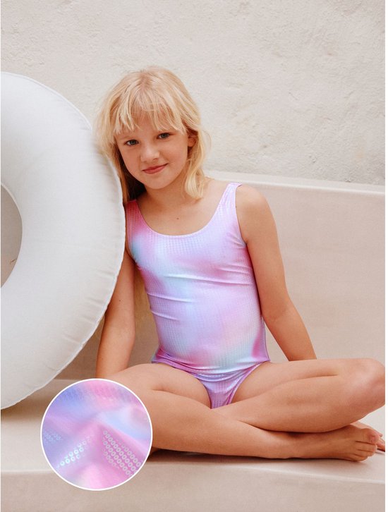 Meisje zittend met veelkleurig badpak met tie-dye print en pailletten.