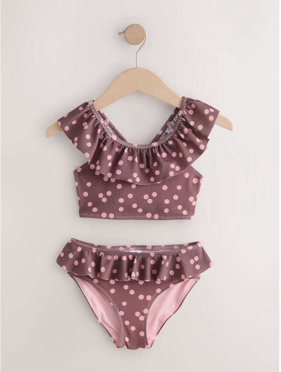 Paarse bikini met roze stippen en ruches, hangt aan een kledinghanger.