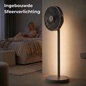 Grijze staande ventilator in een slaapkamer met ingebouwde sfeerverlichting. Vrouw leest boek op bed.