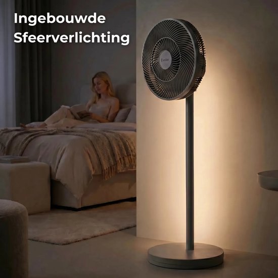 Grijze staande ventilator in een slaapkamer met ingebouwde sfeerverlichting. Vrouw leest boek op bed.