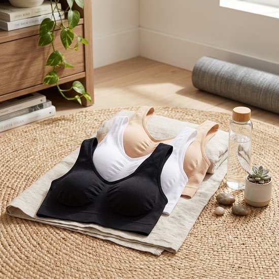 Zwarte, witte en beige sportbeha's op een ronde mat, naast een waterfles.