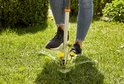 Close-up van schoenen en GARDENA onkruidsteker die paardenbloem uit gras verwijdert.