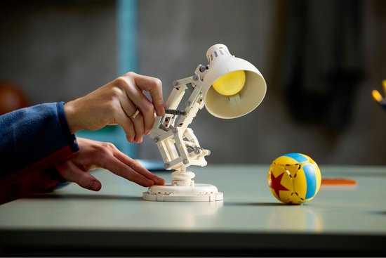 Mains ajustant la lampe blanche LEGO Luxo Jr., ballon à étoile rouge sur la table.