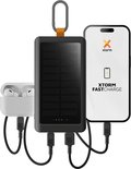 Zwarte Xtorm powerbank met zonnepaneel laadt een smartphone en oordopjes op.