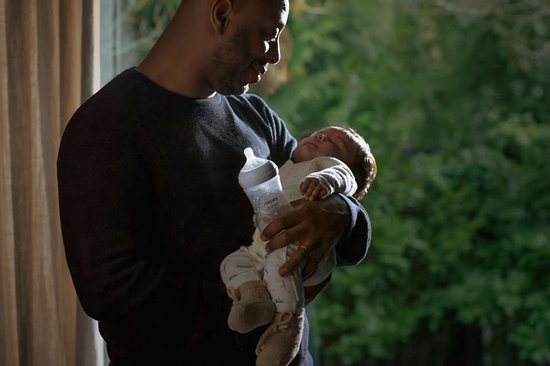 Een man houdt een slapende baby vast en geeft de baby een Philips Avent fles.