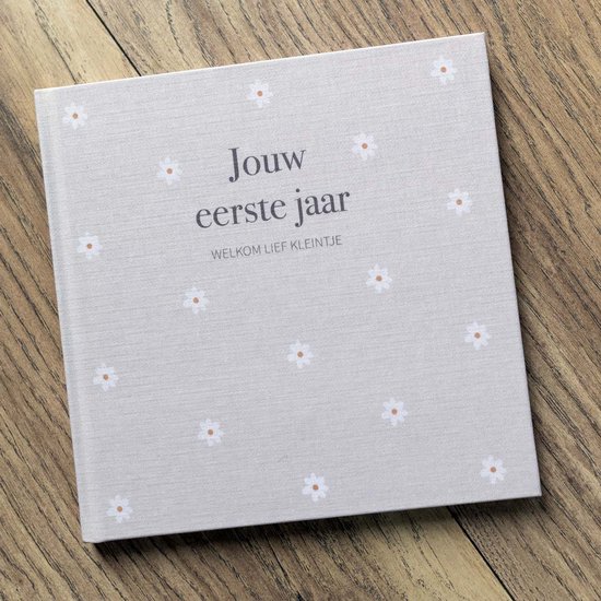Voorzijde van een babyboek met de titel 'Jouw eerste jaar' en kleine madeliefjesprint, liggend op een houten ondergrond.