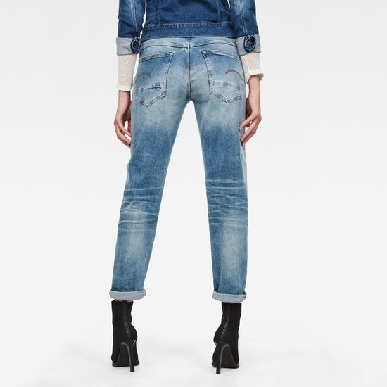 Gedragen achterkant van een vrouw in een lichte, gescheurde jeans met opgerolde broekspijpen en zwarte laarzen.
