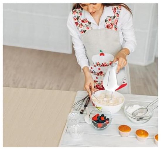 Een vrouw met een schort met bloemenprint mixt ingrediënten met een witte Tefal handmixer.